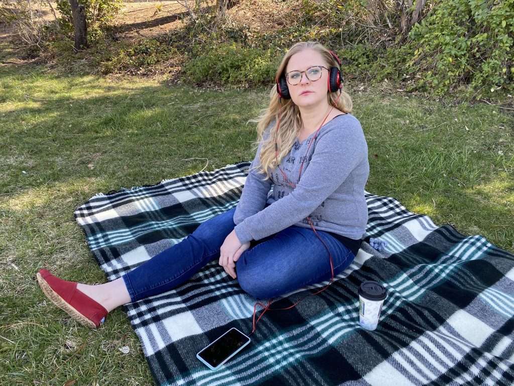 Woman seated on blanket outdoors, wearing headphones