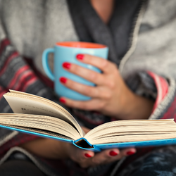 person holding open book and coffee mug